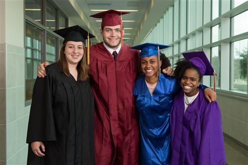 High school Profile of a Graduate committee members pose for a picture in graduation gowns representing each high school. 